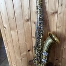 Mosazný saxofon s lakovaným povrchem a stříbrnými klapy. Nástroj vykazuje viditelné opotřebení laku, zejména v horní části trubice a u čňapku. Na těl…