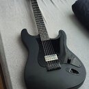 Černá elektrická kytara s matným povrchem a černým pickguardem. Na hlavě hmatníku je viditelné logo Fender. Nástroj má jeden humbucker v pozici kobyl…