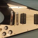 Detail černé elektrické kytary s bílým pickguardem a dvěma humbuckery. Na těle jsou tři oválné ovládací knofíky a jeden přepínač. Povrch kytary vykaz…