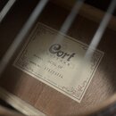 Fotografie zachycuje vnitřek akustické kytary s viditelnou štítkem na dřevěném povrchu. Na štítku je uveden nápis Cort GUITARS, MODEL: AC70 OP a SERI…