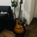 Akustická kytara s korpusem v tmavě hnědém sunburst provedení a dřevěným hmatníkem. Na hlavě nástroje je bílý nápis Fender. Na těle kytary je nalepen…