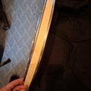 Detailní pohled na hranu kruhového nástroje, pravděpodobně bubnu. Je vidět světlý dřevěný korpus a kovový obruč s viditelným opotřebením povrchu a ox…