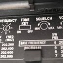 Detailní záběr na černý plastový panel s bílými nápisy a tabulkou frekvencí. Jsou zde uvedeny sekce FREQUENCY, TONE KEY s přepínačem ON/OFF, SQUELCH…