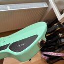 Detail zadní strany světle zelené elektrické kytary. Na těle je černý plastový kryt s bílými symboly CE a dalšími nečitelnými znaky. V pravé části je…