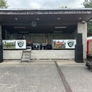 Fotografie zachycuje improvizované venkovní pódium v cihlové stavbě. Na scéně jsou umístěny dvě černé reproduktorové sestavy, několik černých flightc…