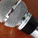 Detailní pohled na horní část dynamického mikrofonu s kovovou síťkou a stříbrným tělem. Na černém kroužku pod hlavou je bílý nápis MODEL 565SD a část…