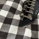 Detail hlavy černé kytary s šesti ladicími mechanismy v černém chromu. Na každém mechanismu je vyryt nápis GROVER. Na hraně hlavy jsou viditelné symb…