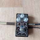 Hnědý efekt pedál s bílým ornamentálním vzorem. Na přední straně jsou tři průhledné oválné knofíky a nápisy MXR CUSTOM SHOP. Pod knofíky jsou nečitel…