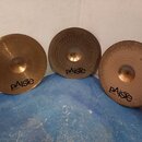 Tři mosazné činely s viditelným klepaním povrchu. Každý z nich má v dolní části černý nápis pAiste a pod ním menší text MADE IN GERMANY. Povrchy čine…