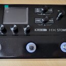 Černý kytarový procesor s nápisem LINE 6 HX STOMP. Zařízení má malý displej, několik ovládacích knoflíků a tři stupňovými spínače v dolní části. Na h…