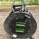 Černý kabelový naviják s několika připojenými kabely a konektory. Na čelní straně jsou dvě řady konektorů s označením Ax1, 2, 3, 4 v horní části a 25…