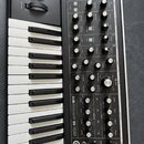 Černý analogový syntetizátor s klaviaturou a dřevěnými bočními panely. Na předním panelu je v bílém nápisu model SUBSEQUENT 25 a logo Moog. Přístroj…