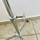 Detail stříbrného kovového stojanu s teleskopickým mechanismem. Na spojovacímu šroubu a okolním kovovém prstenci jsou vidět známky koroze a opotřeben…
