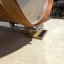 Detailní pohled na spodní část dřevěného bubnu s připevněným dřevěným pedálem. Nástroj má hnědý dřevěný korpus a kovové mechanismy s chromovaným povr…