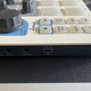 Detailní pohled na zadní panel a část ovládací plochy bílého elektronického zařízení. Na horní části je vidět logo Arturia, nápis LEVEL/RATE a několi…