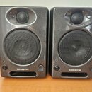 Dva identické studiové monitory v tmavě šedém lesklém provedení. Každý reproduktor má v horní části menší výšký reproduktor a ve spodní části větší b…