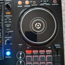 Černý DJ kontrolér s velkým kruhovým jog-colem uprostřed. Na panelu jsou různé tlačítka, posuvníky a nápisy jako HOT CUE, BEAT LOOP, BEAT JUMP, SAMPL…