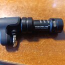 Černý cylindrický mikrofon s integrovaným plastovým držákem a připojeným jack konektorem. Na těle je bílý nápis VIDEOMIC ME™ a pod ním menší text MAD…
