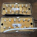 Dvě elektrické snímače s kovovými kryty a šesti viditelnými šrouby na každém. Horní snímač má bílý štítek s nápisy FLT-N-CR, 101, YM47012C a písmenem…