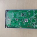 Zelená tiskovaná spoje s elektronickými součástkami umístěná v průhledném plastovém krytu. Na desce jsou bílé nápisy, včetně textu MAIN SHEET ASSY NA…