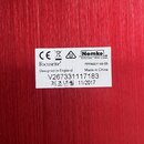 Detailní záběr na bílou papírovou nálepku s technickými údaji nalepenou na červeném povrchu. Na štítku jsou loga CE, symbol přeškrtnuté popelnice a l…