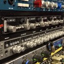Detail rackového vybavení s několika studiovými přístroji. Horní černý přístroj nese logo WARM AUDIO a má popisky 5 - KICK OUT a 6 - SNARE BOTT. Pros…