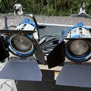 Dvě modré studiové lampy s černými klapkami umístěné na černém transportním kufru. Na těle pravé lampy je viditelný svislý nápis "PAR". Oba spoty maj…