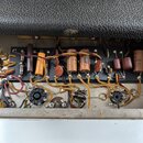 Fotografie zachycuje vnitřek elektronického zařízení s viditelnými komponenty na černé montážní desce. Jsou zde rozmístěny různé typy kondenzátorů a…