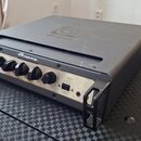 Černý rackový zesilovač s kovovým předním panelem stříbrné barvy. Na panelu je nápis Ampeg a vlevo označení SVT-4 Pro. Jsou zde čtyři černé oválné ov…