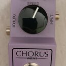 Fialový efekt pedál s nápisem CHORUS MINI. Na horní části jsou dva malé černé oválné knoflíky s popisky DEPTH a LEVEL, uprostřed velký černý kruhový…