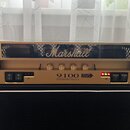 Zlatý kytarový zesilovač s černým chassis a černým reproduktorem v dolní části. Na horním panelu je nápis 9100 a Dual MonoBloc Amplifier, vedle něj l…