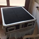 Černý transportní kufr s hliníkovým profilem a kovovými rohy. Na přední straně jsou tři kovové úchyty. Povrch je potažen černým materiálem, který vyk…