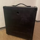 Fotografie znázorňuje zadní stranu černého komba s rukojetí v horní části. Povrch je z texturovaného materiálu a vykazuje drobné oděrky a zaprášení.…