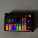 Černý zvukový mixér s řadou barevných tlačítek a ovládacích prvků. Na horní části jsou čtyři černé otočné knoflíky s popisky -TREBLE+, -MID +, -BASS…