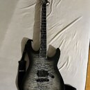 Elektrická kytara s černým korpusem a topem z vyvzorovaného dřeva v šedé barvě. Na hlavě hmatníku je viditelné logo ESP. Kytara má dva humbuckery, je…