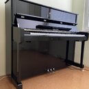 Černý digitální piano v podobě pianina s glossy povrchem. Nad klávesnicí je umístěn nápis "Pitmanmiller". Nástroj má tři pedály a v horní části je zr…