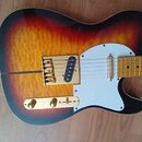 Elektrická kytara s tlemem v barvách sunburst a výraznou dřevěnou strukturou. Nástroj má bílý pickguard, zlaté potenciometry a zlatý hardware včetně…