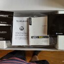 V otevřené krabici s polystyrenovými výplněmi je umístěn procesor vokálních efektů stříbrné barvy s nápisem VoiceWorks a logem TC HELICON. Vedle přís…