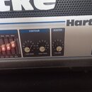 Detail ovládacího panelu zesilovače značky Hartke. Panel obsahuje sekci EQUALIZER s posuvníky, sekci CONTOUR s knoflíky LOW PASS a HIGH PASS a sekci…