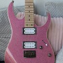 Elektrická kytara s růžovým třpytivým povrchem těla a hnedem dřevěným hmatníkem. Nástroj má dva humbuckery a fixní most s nápisem "Tune-o-matic". Na…