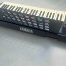 Černý elektronický klavír s bílými a černými klávesami. Na přední straně je bílý nápis YAMAHA a v pravém horním rohu menší nápis YAMAHA. Vpravo jsou…