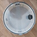 Fotografie znázorňuje bílý buben s kovovým obručováním a napnutou blánou. Na bláně je vpravo černé logo MAPEX a vlevo nápis UX SERIES / MADE IN TAIWA…