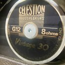 Fotografie detailu reproduktoru s černým středovým krytem a zlatými nápisy. Na krytu je uvedeno logo CELESTION LOUDSPEAKERS, označení G12, 8ohms a mo…