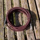 Svinutý instrumentální kabel s červeně a černě pleteným opláštěním. Na jednom z černých konektorů je viditelný bílý nápis "Fender". Kabel má na obou…