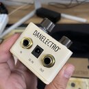 Bílý efekt pedál s nápisem DANELECTRO®. Na horní straně jsou dva kovové ovládací knofíky a na přední straně se nacházejí dva zlaté konektory s popisk…
