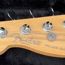 Fotografie zachycuje hlavu basové kytary z přírodního světlého dřeva s chromovanými ladicími kolíky. Na dřevě je vidět černé logo Fender, nápis MADE…