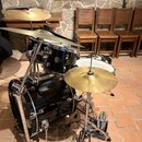 Černá bicí souprava s chromovaným hardwarem. Na basovém bubnu je viditelné logo GRETSCH. Souprava obsahuje basový buben, dva tom-tomy, malý buben a t…