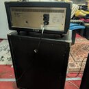 Zadní strana kytarového komba umístěného na černém reproduktorovém boxu. Na horním přístroji je stříbrný štít s nápisy „VES Musikelektronik Klingenth…