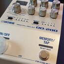 Bílý efekt pedál s nápisy BOSS DIGITAL DELAY DD-200. Na horní části jsou ovládací knoflíky a přepínače s popisy funkcí, jako je TAP DIVISION nebo MEM…