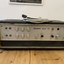 Černý kytarový kombozesilovač s bílým předním panelem a kovovým rámem. Na panelu je nápis Austrovox Reverb 100 a řada ovládacích knoflíků s popisky i…